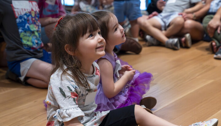 A close-up of two smiling White children sitting on the floor of a Carter gallery.