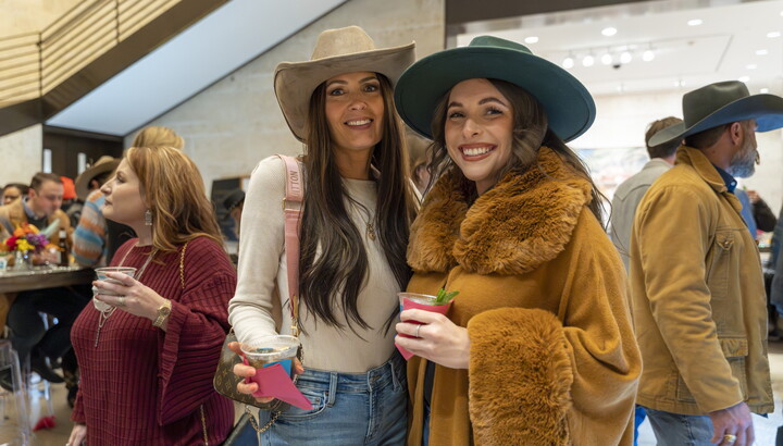 Two-light-skinned women stand side-by-side in the Carter's Atrium, both wearing cowboy hats and holding drinks.