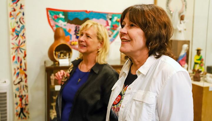 Two smiling White women look at art in an artist's studio.