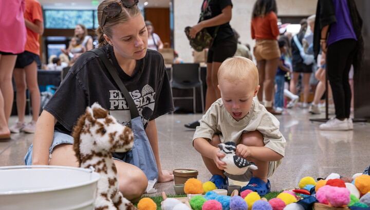 A White woman and small child on the floor of the Carter Atrium playing with colorful pompoms.