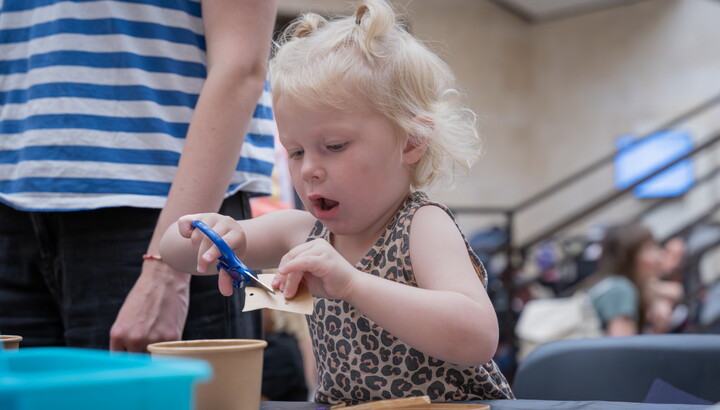 A White toddler uses safety scissors to cut paper while making an art project in the Carter's Atrium.