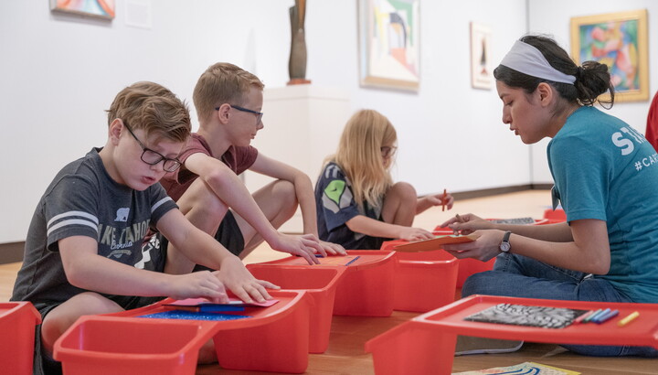 Three middle-school age children and a Carter educator sit on the floor of a gallery making art.