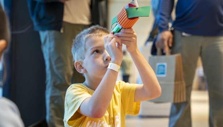 A White child looks in a tube made from colored construction paper in the Carter's Atrium.