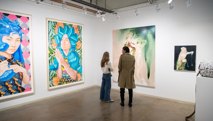 Two people stand in an art gallery looking at large-scale artworks.