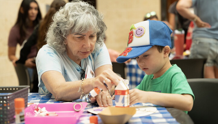 An older White woman helps a young White child make art at a table in the Carter's Atrium.
