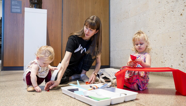 A White woman and two small children play with art supplies on the floor of a Carter gallery.