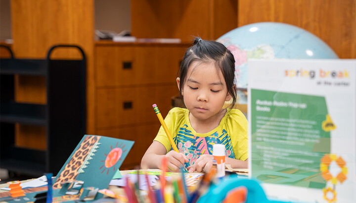 A young child with Asian features is focused on making art in the Carter's Library.