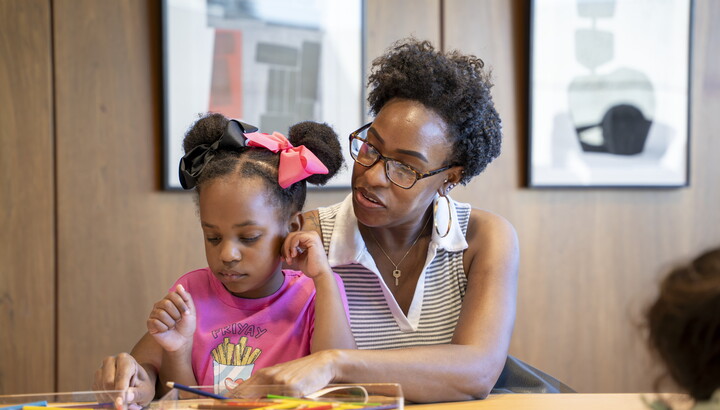 A Black woman and the child on her lap make art in the Carter's Family Pop-Up Space.