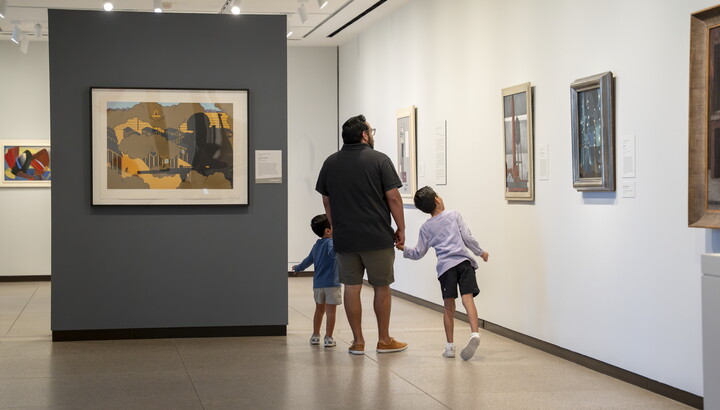 A White man holds hands with two small children as the look at art in the Carter galleries.