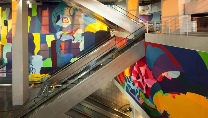 Stairways and escalators surrounded by walls covered in colorful murals.
