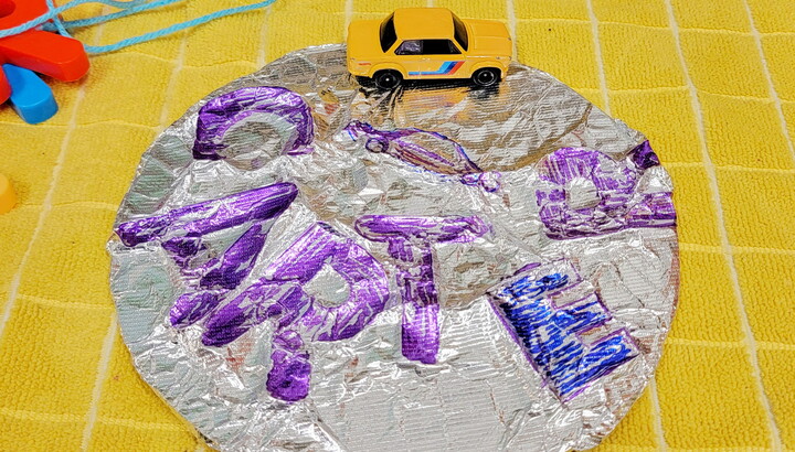 A circular foil artwork with colored impressions of letters lays on a table.