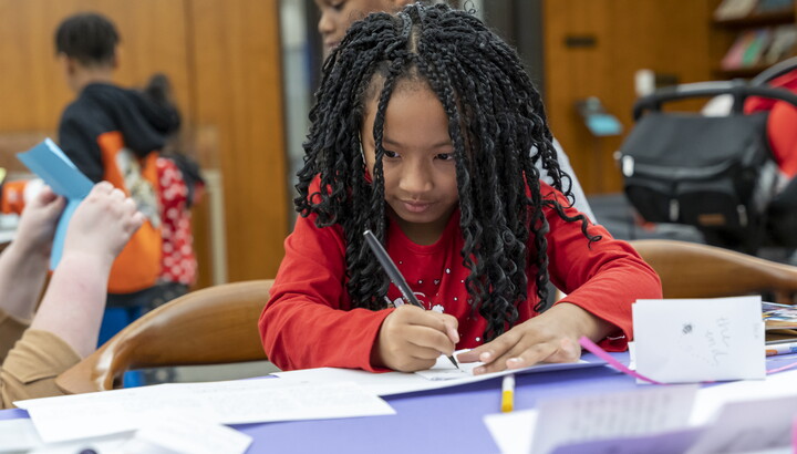A dark-skinned child with long hair draws at a table in the Carter's Family Pop-up Space.