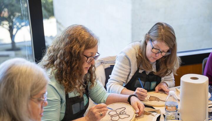 Three White women are seated at a table in the Carter's Lounge making art together.