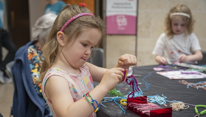 A young White child uses yarn and colored pipe cleaners to make art at a table in the Carter's Atrium,