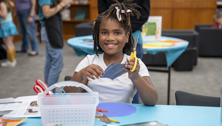 A smiling pre-teen Black girl makes art at a table in the Carter's Family Pop-up Space.