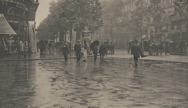 A black-and-white photograph of people crossing a city street in the rain.