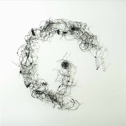 A wall sculpture of delicate twigs and stems arranged to make a shape like an uppercase G.