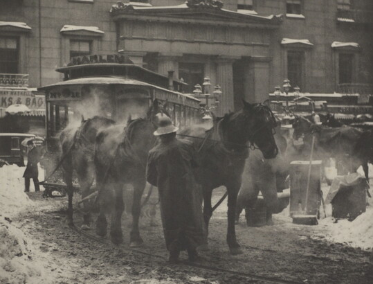A black-and-white photograph of horses pulling a trolley on a busy street covered with slush and snow.