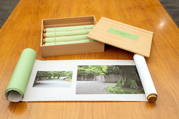 A wood box containing four green scrolls and a fifth partially unrolled scroll on a wood table.