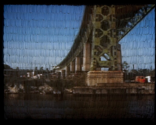 A video still of the underside of a bridge projected onto a wall covered in white feathers.