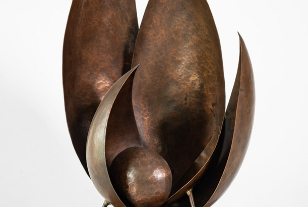 A bronze sculpture with leaf-like shapes reaching upward and a sphere cradled at the bottom of the flat, broad leaves.