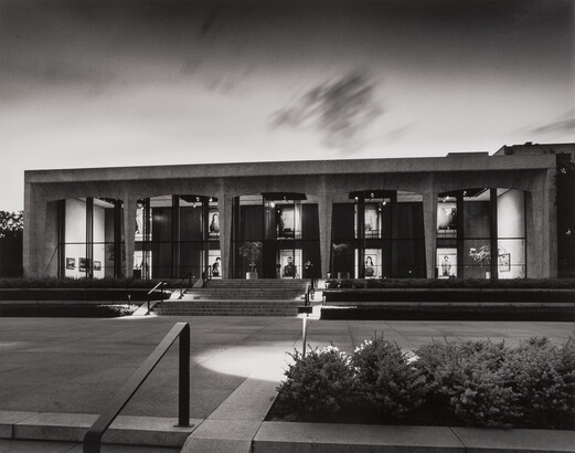 A black-and-white photograph of the facade of the Carter at dusk; large-scale portrait photographs can be seen through the Carter&#039;s windows.