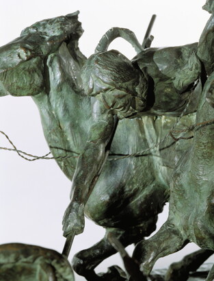 A bronze sculpture of two horses in mid-gallop, with both riders lunging toward a crouching man behind a shield.