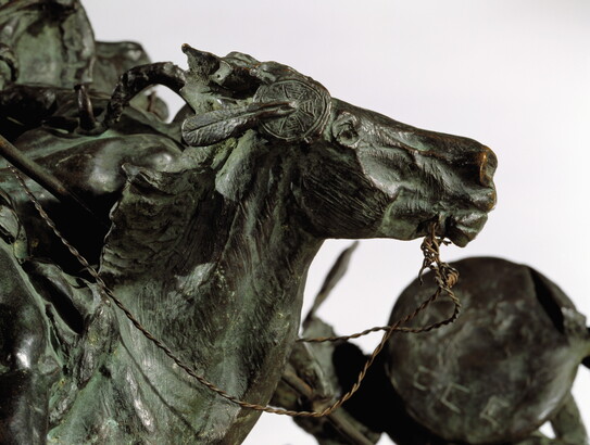 A bronze sculpture of two horses in mid-gallop, with both riders lunging toward a crouching man behind a shield.