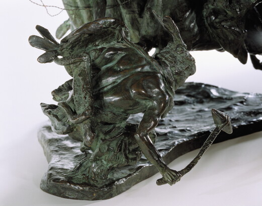 A bronze sculpture of two horses in mid-gallop, with both riders lunging toward a crouching man behind a shield.