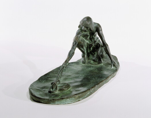 A bronze sculpture of a squatting Indigenous man holding a stick in his outstretched arm toward a snake on the ground.