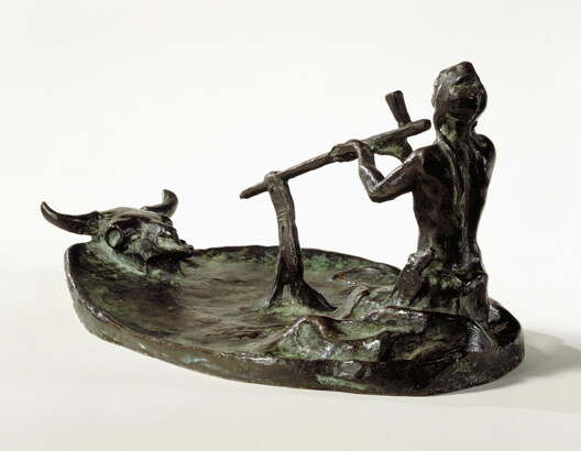 A bronze sculpture of a kneeling Native American man smoking a pipe in front of a bison skull.