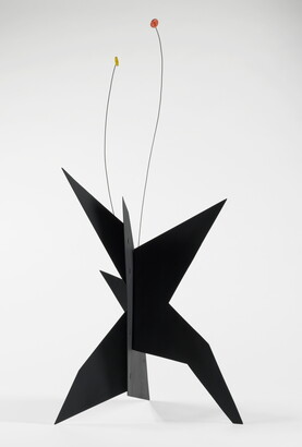 A black, metal, star-like shaped sculpture with two wires rising from the top, one capped with a yellow circle and the other with an orange circle.