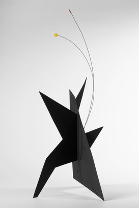 A black, metal, star-like shaped sculpture with two wires rising from the top, one capped with a yellow circle and the other with an orange circle.