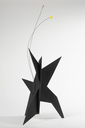 A black, metal, star-like shaped sculpture with two wires rising from the top, one capped with a yellow circle and the other with an orange circle.