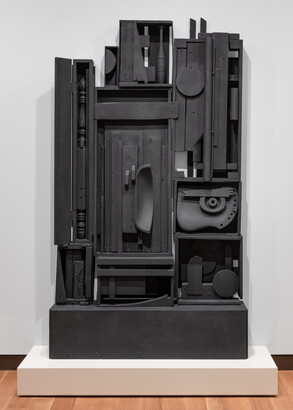 A black-painted wood sculpture with many compartments that include fragments of things such as a bedpost, juggling pin, and a chair.