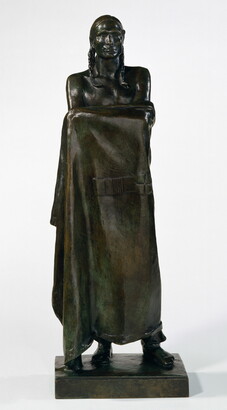 A bronze sculpture of a Native American man who stands wrapped in a blanket.