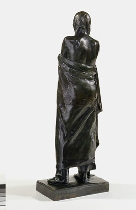 A bronze sculpture of a Native American man who stands wrapped in a blanket.