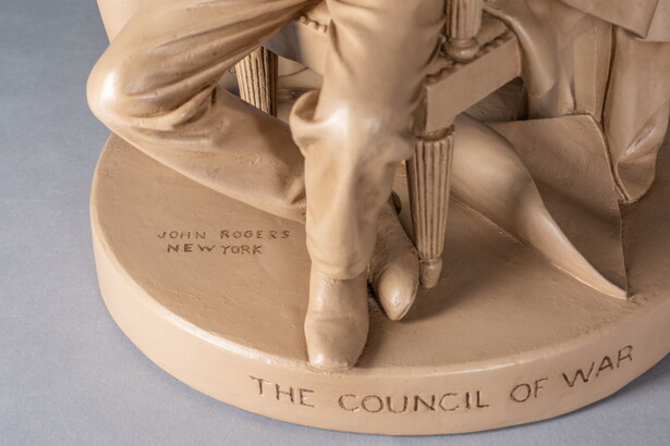 A detail of a sculpture of Abraham Lincoln reading a paper and seated in between two standing men.