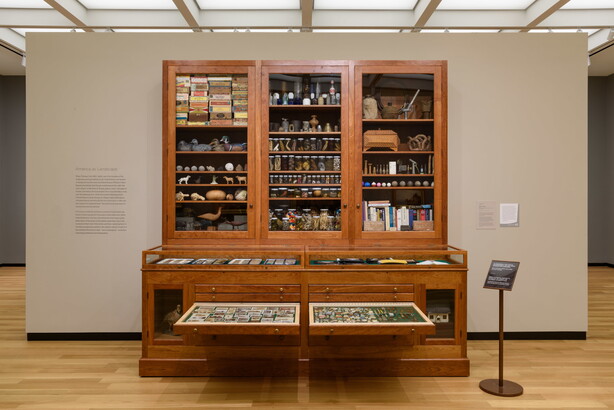 A large wooden cabinet with drawers on the bottom half and glass-fronted cabinets above, all filled with random objects.