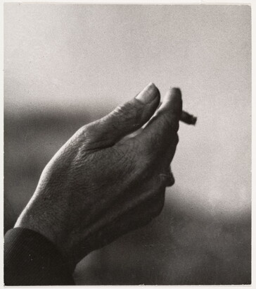 A black-and-white close-up photograph of a right hand holding an almost-finished cigarette.