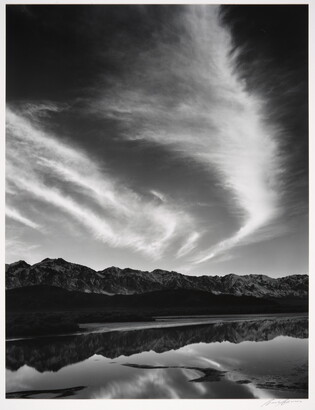 A black-and-white landscape photograph of mountains and clouds that reflect on the still water in the foreground.