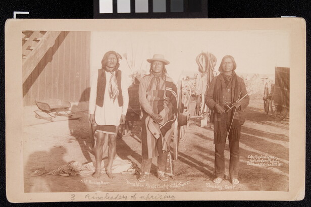 A sepia-toned photograph of three Indigenous men standing outside next to each other.