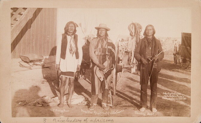 A sepia-toned photograph of three Indigenous men standing outside next to each other.