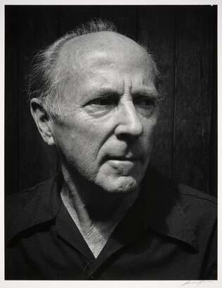 A black-and-white photograph of the head and shoulders of an older balding White man wearing a dark button-down shirt, head turned slightly.