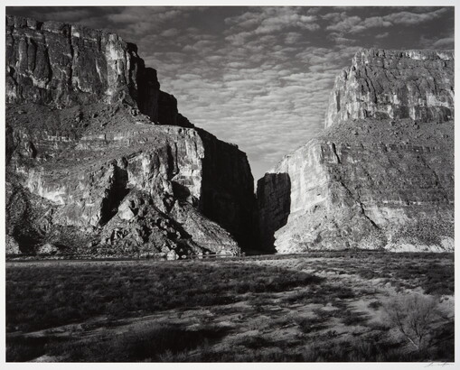 A black-and-white photograph of a canyon between two large mountains.