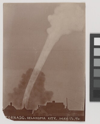 A sepia-toned photograph of a white funnel cloud above the silhouette of a town.