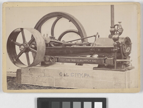 A black-and-white photograph of a machine with two wheels of varying sizes sitting on a concrete base.