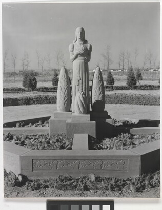 A black-and-white photograph of a stone statue of a stylized figure standing between stylized stone trees.