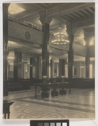 A black-and-white photograph of the interior of an ornate office lobby with inlaid floors, columns, and chandeliers.