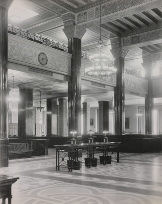 A black-and-white photograph of the interior of an ornate office lobby with inlaid floors, columns, and chandeliers.